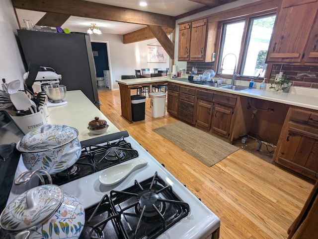 kitchen with light wood-type flooring, tasteful backsplash, gas range gas stove, sink, and beamed ceiling