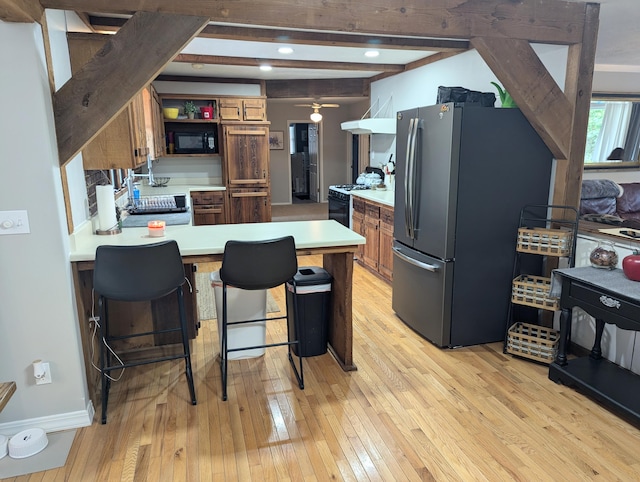 kitchen with black appliances, beam ceiling, light hardwood / wood-style floors, a kitchen bar, and kitchen peninsula