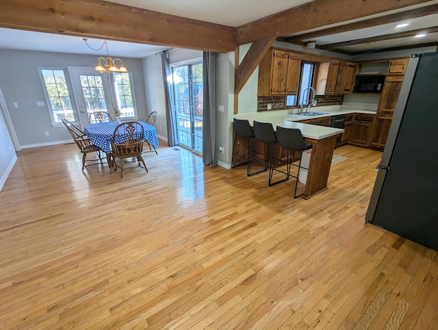 dining area with sink, beamed ceiling, a notable chandelier, and light wood-type flooring