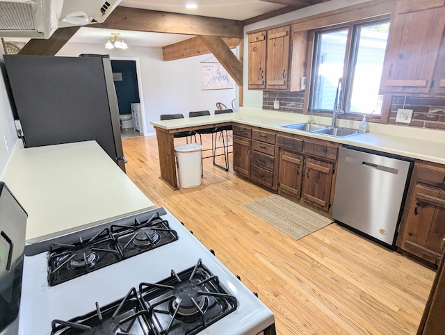 kitchen featuring sink, decorative backsplash, beamed ceiling, light hardwood / wood-style floors, and stainless steel appliances