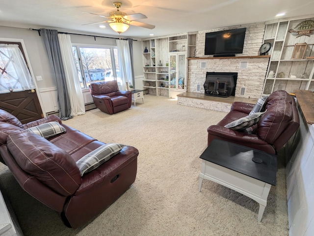 carpeted living room featuring a stone fireplace, ceiling fan, built in features, and a baseboard heating unit