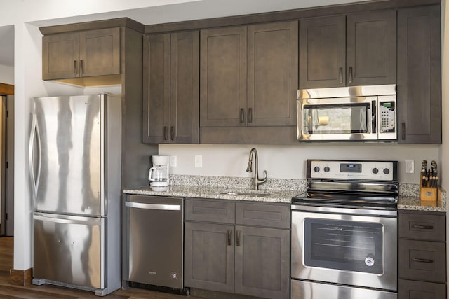 kitchen featuring dark brown cabinetry, sink, appliances with stainless steel finishes, dark hardwood / wood-style floors, and light stone countertops