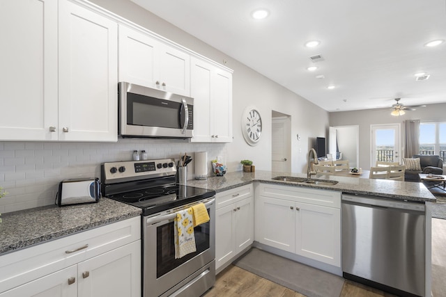 kitchen featuring wood-type flooring, sink, kitchen peninsula, appliances with stainless steel finishes, and white cabinetry