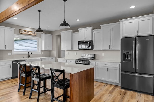 kitchen with a center island, decorative light fixtures, light hardwood / wood-style floors, white cabinetry, and stainless steel appliances