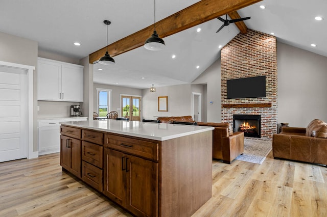 kitchen with white cabinetry, hanging light fixtures, vaulted ceiling with beams, light hardwood / wood-style flooring, and an island with sink