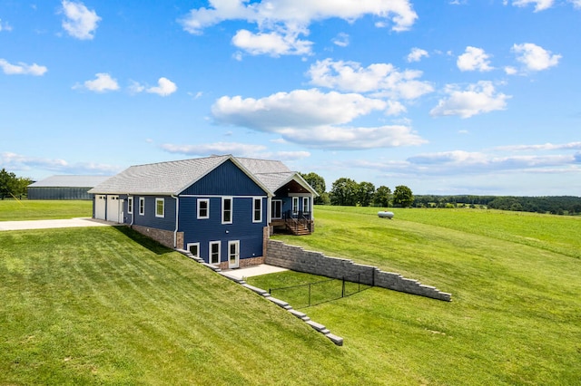 view of side of home featuring a yard, a deck, a rural view, a garage, and an outbuilding