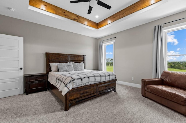 bedroom featuring a tray ceiling, baseboards, multiple windows, and light colored carpet