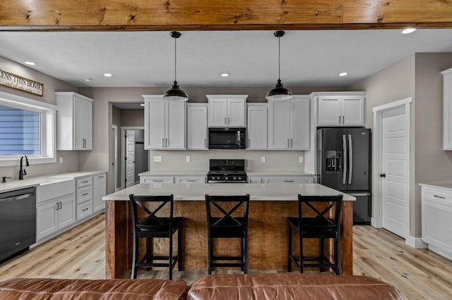 kitchen featuring a breakfast bar area, white cabinetry, black appliances, and light wood-type flooring