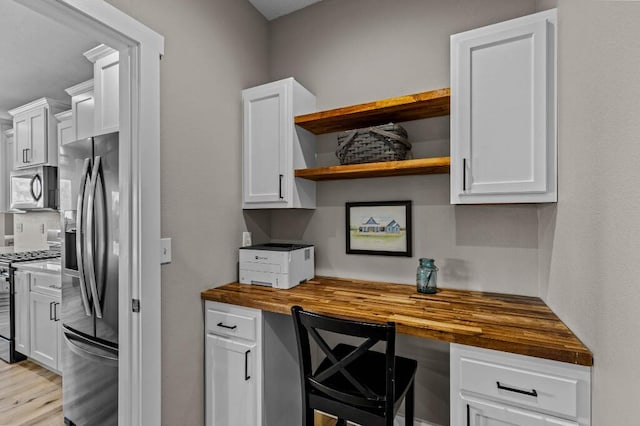 kitchen featuring butcher block counters, stainless steel appliances, white cabinets, built in study area, and open shelves