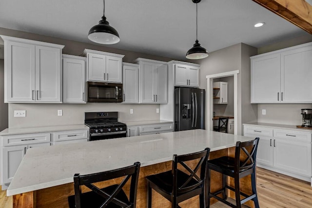 kitchen with white cabinetry, black appliances, a kitchen breakfast bar, and light wood-type flooring