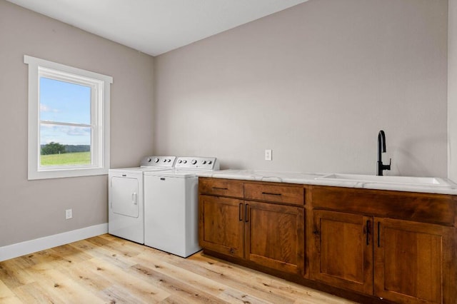 laundry area with light wood-type flooring, a sink, washing machine and dryer, cabinet space, and baseboards