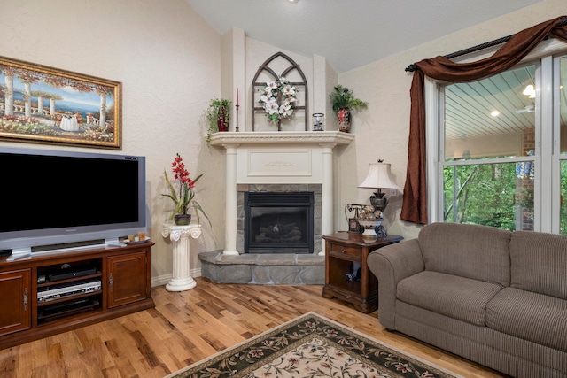 living room featuring lofted ceiling, a stone fireplace, and hardwood / wood-style floors