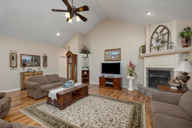 living room featuring wood-type flooring, lofted ceiling, a tiled fireplace, and ceiling fan