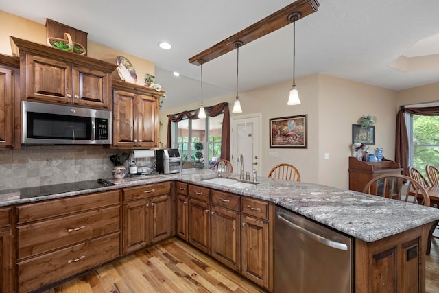 kitchen with light wood-type flooring, light stone counters, kitchen peninsula, appliances with stainless steel finishes, and decorative light fixtures