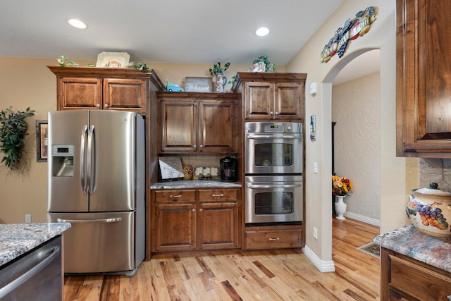 kitchen with light stone countertops, stainless steel appliances, light hardwood / wood-style flooring, and decorative backsplash