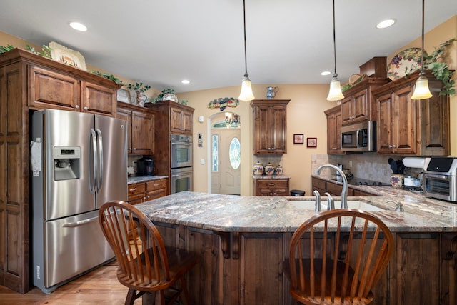 kitchen with light stone countertops, decorative backsplash, stainless steel appliances, pendant lighting, and light hardwood / wood-style flooring