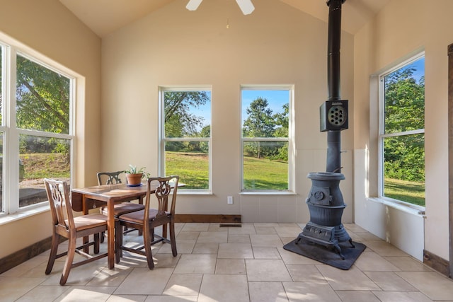 tiled dining space featuring ceiling fan, high vaulted ceiling, a wood stove, and a healthy amount of sunlight