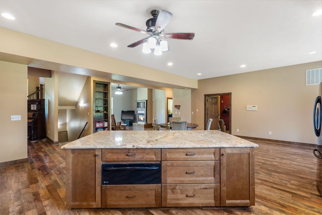 kitchen featuring ceiling fan, dark hardwood / wood-style flooring, a center island, and light stone counters