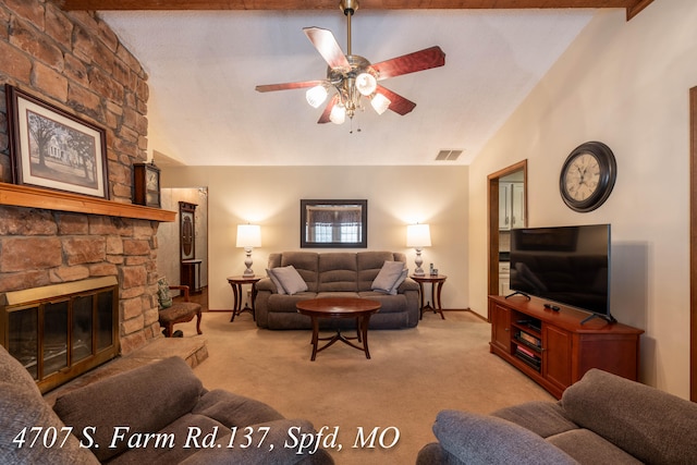 carpeted living room with ceiling fan, lofted ceiling with beams, and a stone fireplace