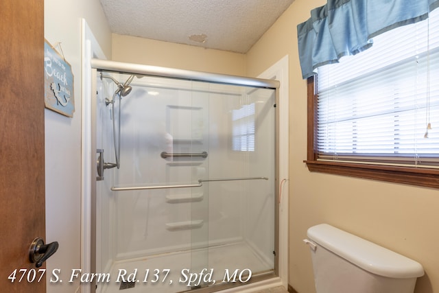 bathroom featuring a shower with shower door, toilet, and a textured ceiling