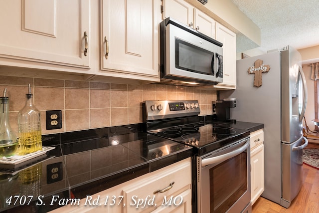 kitchen with a textured ceiling, stainless steel appliances, backsplash, and light hardwood / wood-style flooring