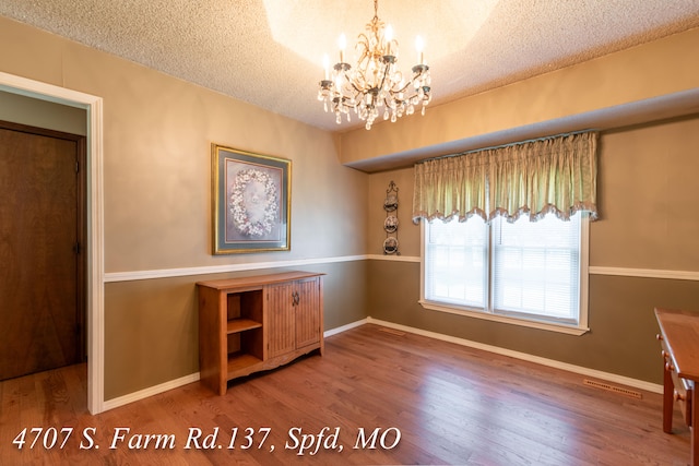 unfurnished dining area with a notable chandelier, a textured ceiling, and hardwood / wood-style floors