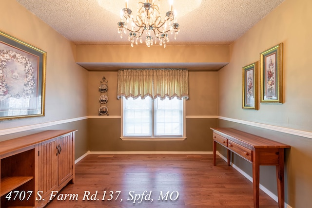 unfurnished dining area with a notable chandelier, a textured ceiling, and hardwood / wood-style floors