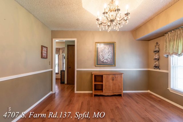 unfurnished dining area with hardwood / wood-style flooring, an inviting chandelier, and a textured ceiling