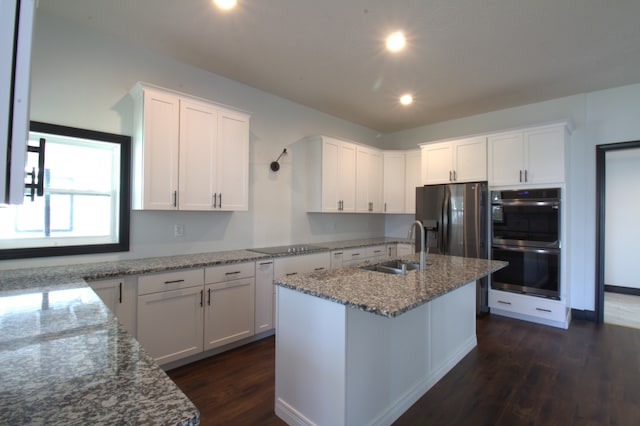 kitchen featuring a center island with sink, black double oven, stainless steel fridge with ice dispenser, and white cabinetry