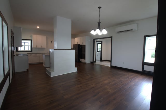 kitchen with a wall mounted air conditioner, white cabinets, dark wood-type flooring, black refrigerator, and hanging light fixtures