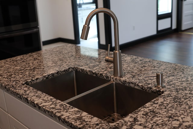 interior details with double oven, dark stone counters, hardwood / wood-style floors, and sink