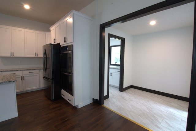 kitchen with white cabinets, double oven, light stone countertops, black refrigerator, and dark hardwood / wood-style flooring