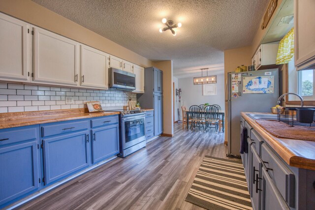 kitchen with stainless steel appliances, tasteful backsplash, wood finished floors, blue cabinetry, and wooden counters