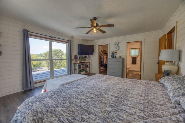 bedroom featuring a spacious closet, wood walls, wood finished floors, and a textured ceiling
