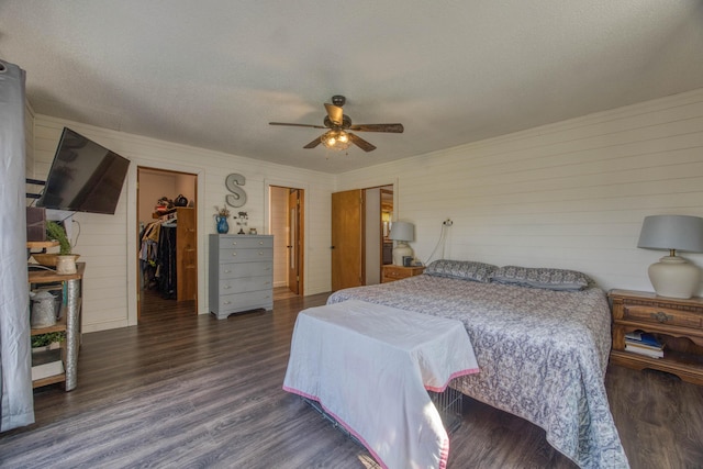bedroom with a ceiling fan, wood finished floors, a textured ceiling, a spacious closet, and wooden walls
