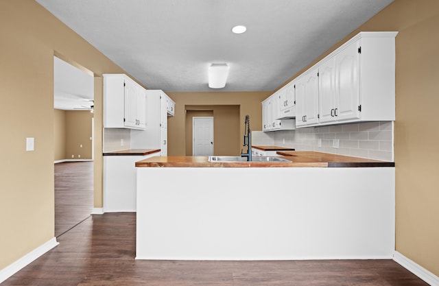 kitchen with wooden counters, tasteful backsplash, kitchen peninsula, dark hardwood / wood-style floors, and white cabinetry