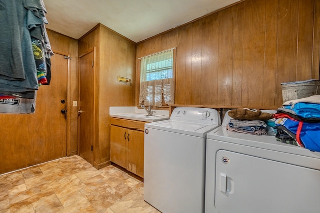 laundry area featuring wood walls, cabinets, independent washer and dryer, and sink