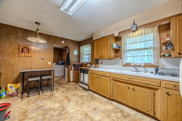 kitchen with washer / dryer, hanging light fixtures, wooden walls, and sink