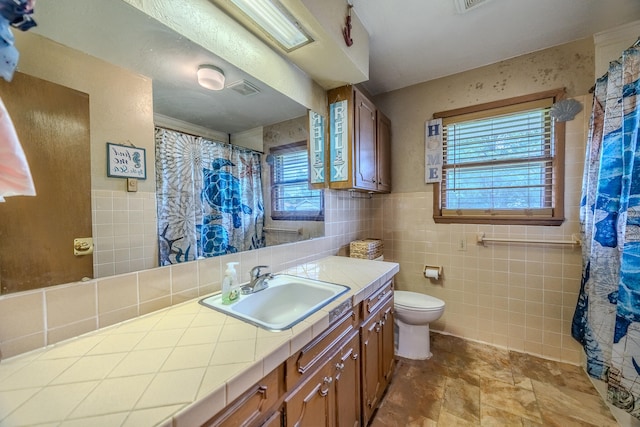 bathroom featuring vanity, toilet, tile walls, and a wealth of natural light