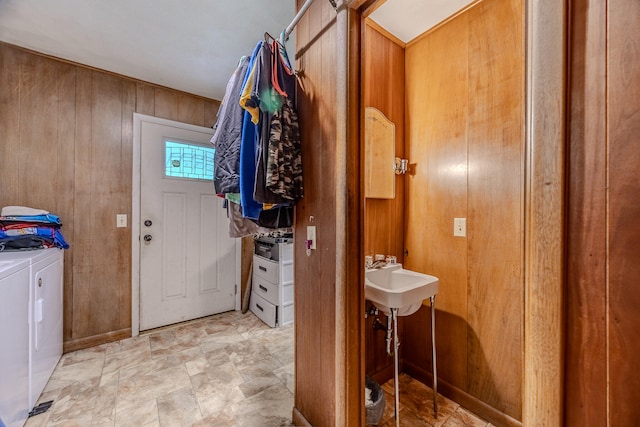 bathroom with washing machine and clothes dryer, wooden walls, and sink