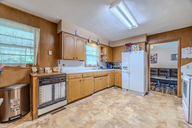 kitchen with wooden walls, sink, a healthy amount of sunlight, and white appliances