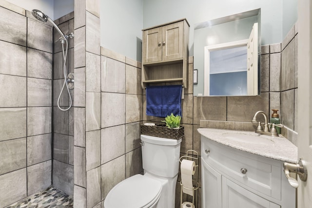 bathroom featuring vanity, tiled shower, toilet, and tile walls