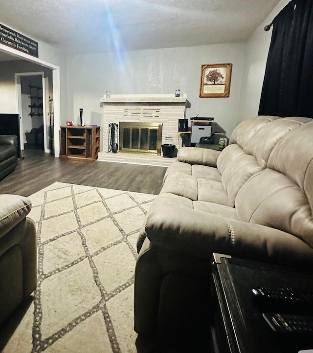 living room with a stone fireplace, wood-type flooring, and a textured ceiling