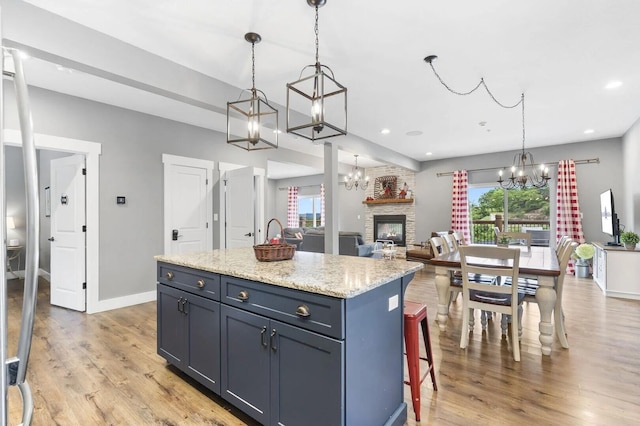 kitchen with a kitchen island, light hardwood / wood-style floors, a fireplace, decorative light fixtures, and a kitchen breakfast bar