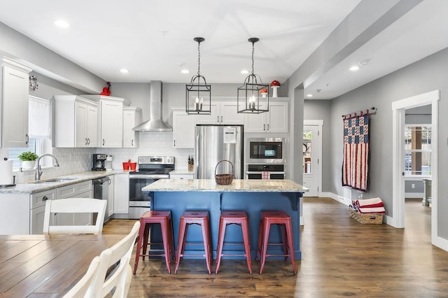 kitchen with wall chimney exhaust hood, plenty of natural light, sink, stainless steel appliances, and a center island