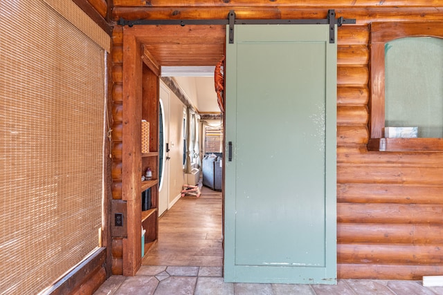 corridor featuring a barn door, light hardwood / wood-style floors, and rustic walls