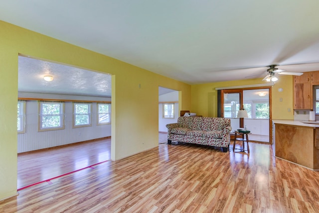 living room featuring light hardwood / wood-style flooring, a textured ceiling, and ceiling fan