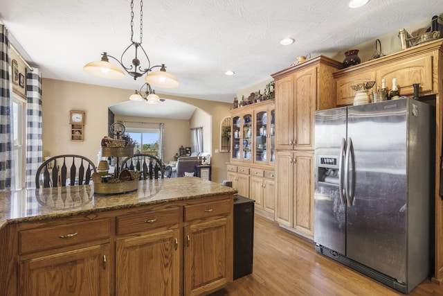 kitchen with hanging light fixtures, stainless steel fridge, light hardwood / wood-style flooring, an inviting chandelier, and dark stone counters