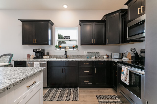 kitchen with light stone counters, white cabinets, sink, appliances with stainless steel finishes, and light hardwood / wood-style floors