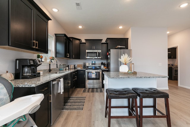 kitchen with light stone countertops, appliances with stainless steel finishes, light wood-type flooring, and sink